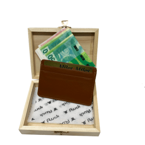 ארנק כרטיסים חום מעור איכותי מונח בתוך קופסת עץ עם שטרות כסף וכרטיס אשראי.