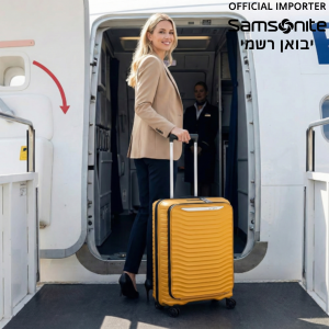אישה בלונדינית לבושה בסטייל עולה למטוס עם מזוודת טרולי צהובה של סמסונייט (Samsonite).