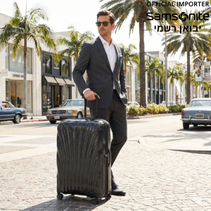 גבר אלגנטי בחליפה ומשקפי שמש הולך ברחוב יוקרתי בלוס אנג'לס עם מזוודת סמסונייט C-Lite שחורה.