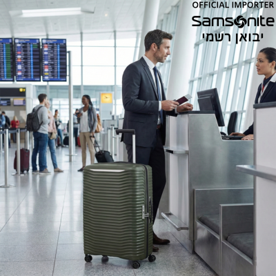 גבר עומד בדלפק צ'ק-אין בשדה תעופה עם מזוודת סמסונייט (Samsonite) קשיחה בצבע ירוק זית.