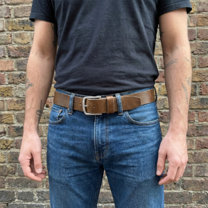 דוגמן עם קעקועים לבוש בג'ינס כחול וטי-שירט שחורה עם חגורת עור חומה ואבזם כסוף בסגנון קז'ואל.