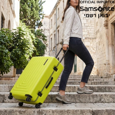 אישה גוררת מזוודה קשיחה בצבע ירוק ליים בולט במעלה מדרגות אבן בסמטה עתיקה.