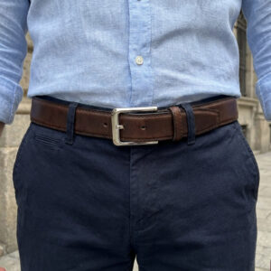 תקריב של גבר לובש חולצה כחולה בהירה, מכנסיים כחולים כהים וחגורת עור חומה איכותית עם אבזם כסוף מלבני.